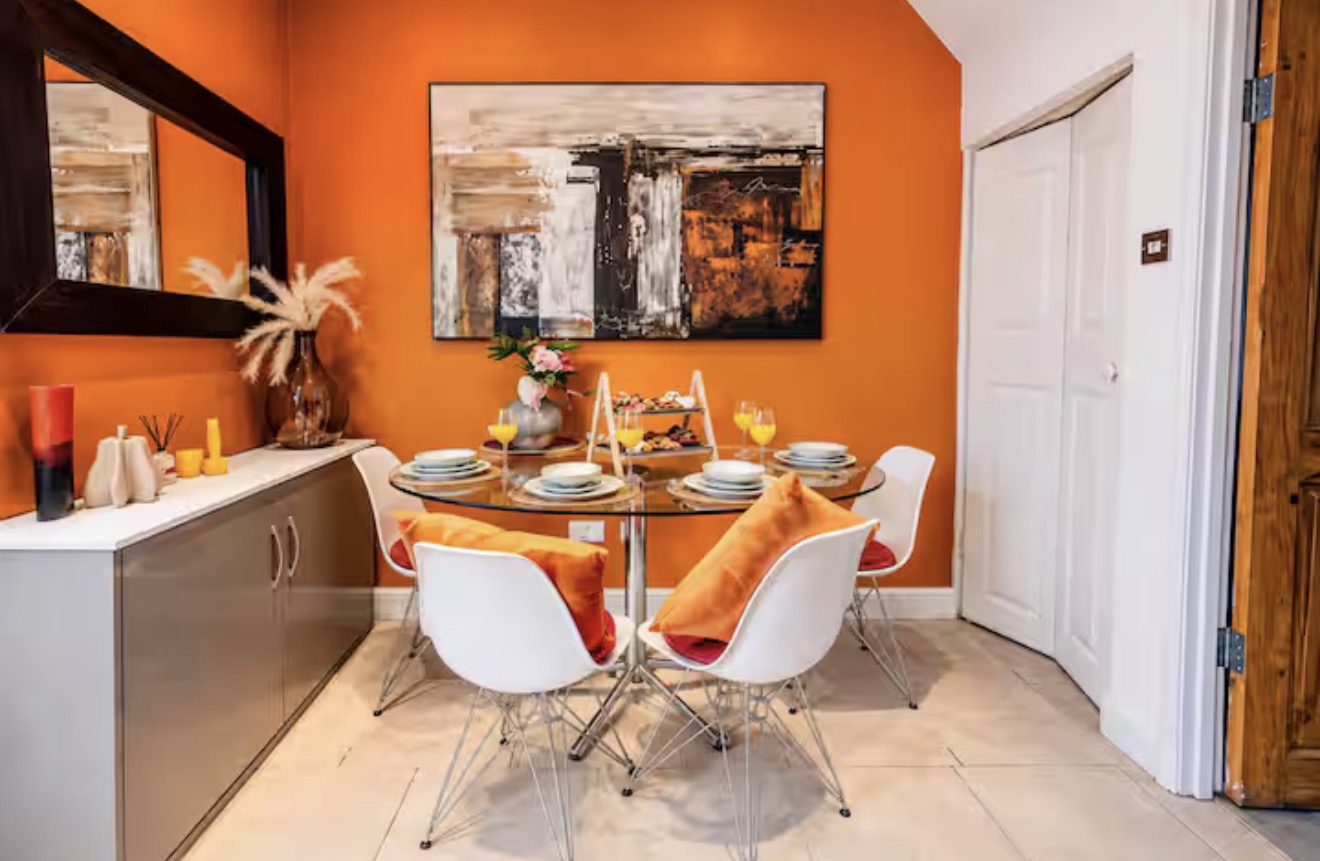 Dining table set for four against a vibrant orange wall